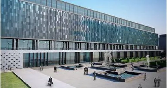 Vue aérienne de complexe de bâtiments modernes avec toiture verte, parkings, routes d'accès et espaces verts environnants.